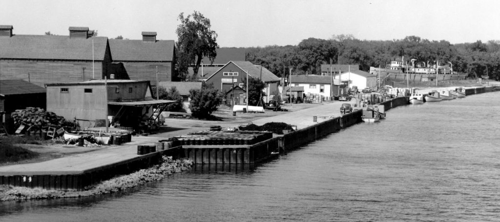 This is a black and white photo of the Selkirk docks in 1957. There are down the road and fishing boats docked.