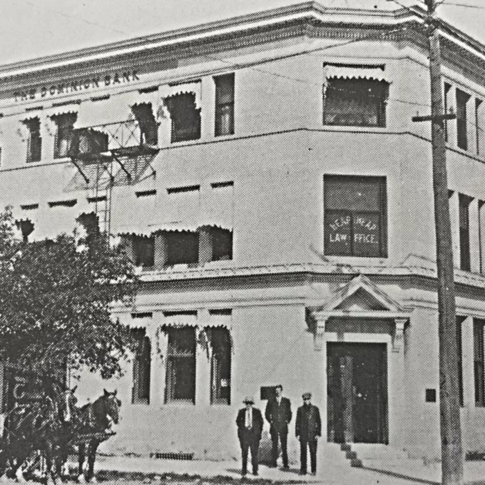The Dominion Bank, 1913, Archives of Manitoba Black and white picture of 3 men in suits standing in front of the Dominion Bank