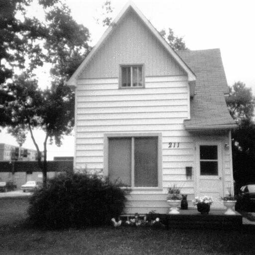 211 McLean, Date Unknown, Selkirk Museum Collection A black and white image of small, narrow house which has a large window at the bottom and a smaller window on the second floor. The door is on the right