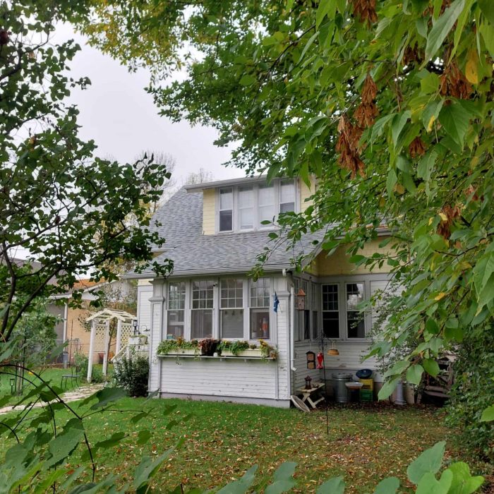 Colour image of a house through vines and trees. The house is yellow