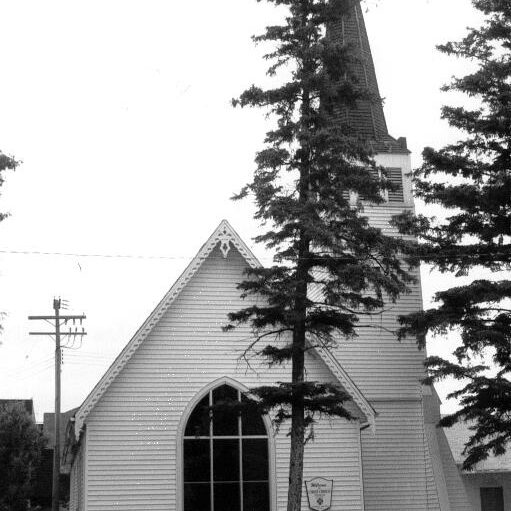 227 McLean, Date Unknown, Selkirk Museum Collection A black and white image of a church with a large steeple to the right. There are two evergreen trees to the right