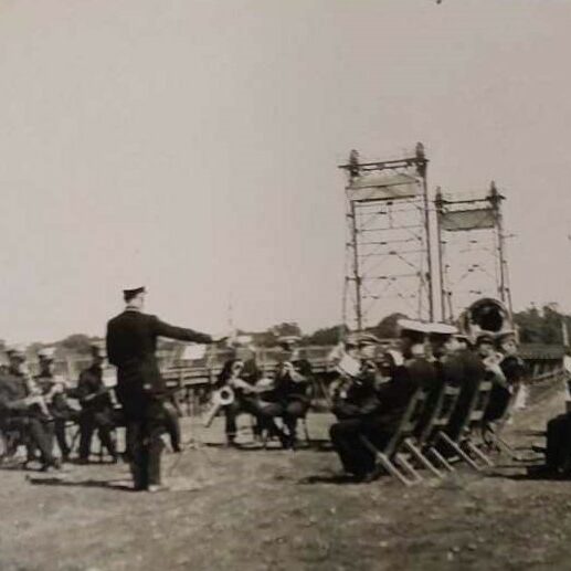 Group of musicians playing in Queen's Park. The Blue Bridge can be seen in the background