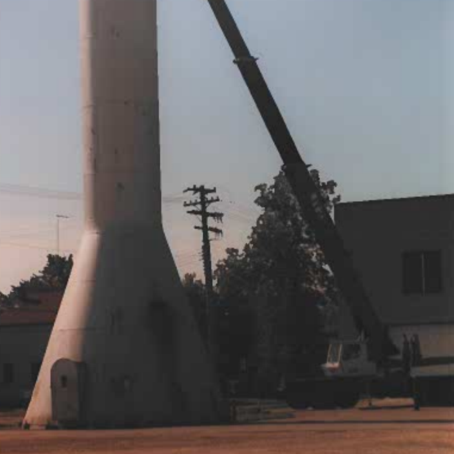 Colour photo of the base of the selkirk water tower. There is a crane truck parked to the right and the crane arm is extended