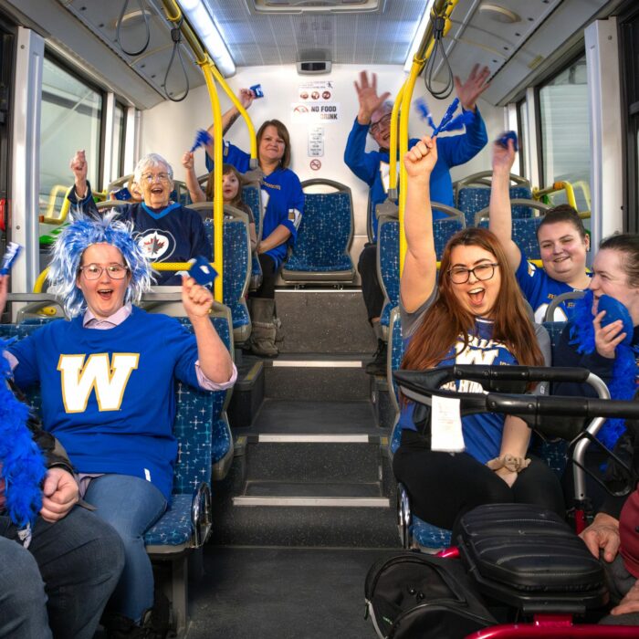 Photo is of a bus full of people wearing Bombers jerseys and holding their arms in the air