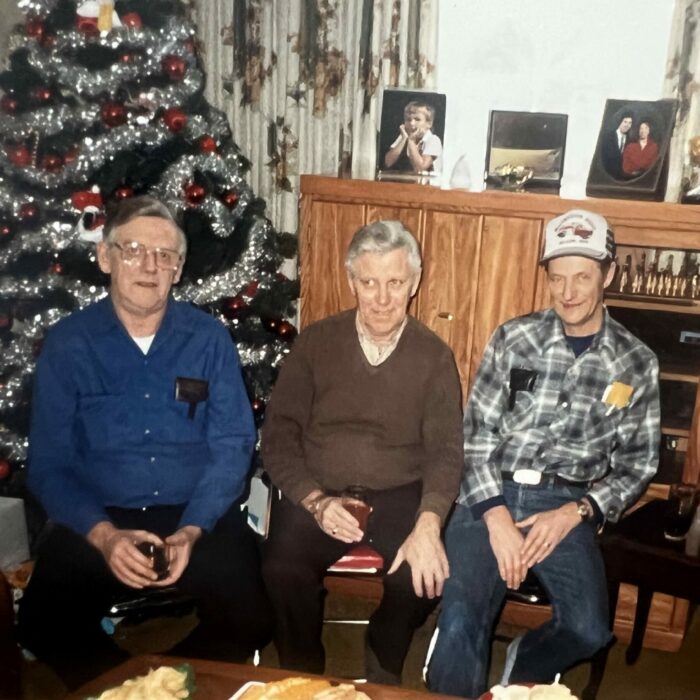 Colour photo of three men sitting in front of a Christmas tree