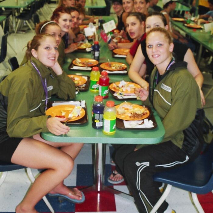 Group of people sit at a cafeteria table. The table is full of food