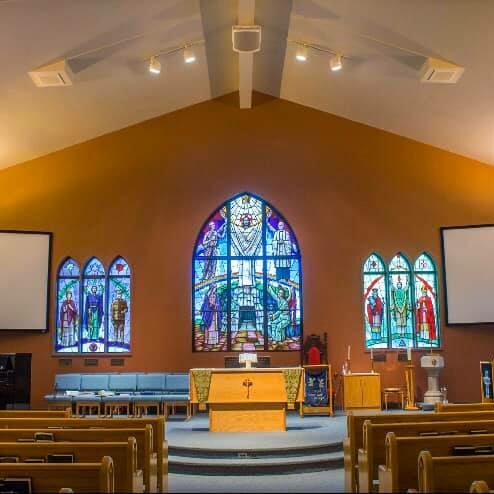 Interior of Christ Church showing three of the many stained glass windows. Pews and projector screens can be seen