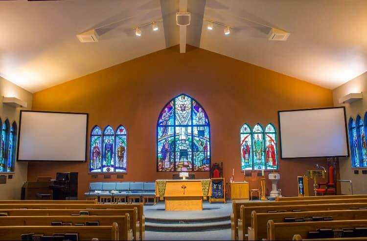 Interior of Christ Church showing three of the many stained glass windows. Pews and projector screens can be seen