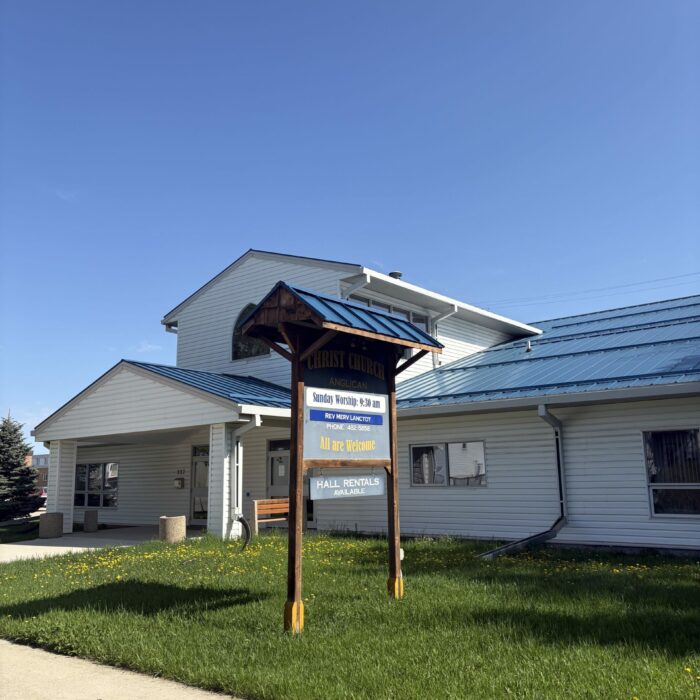 Colour photo of Christ Church exterior. The building is white with a blue tin roof. There is a sign at the front of the building