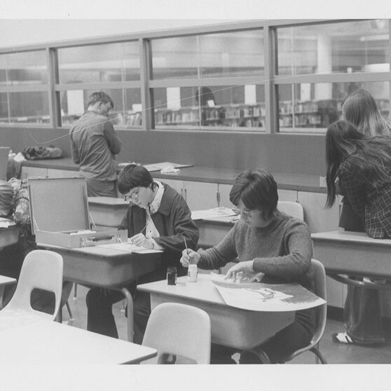 Black and white photo of students painting at their desks