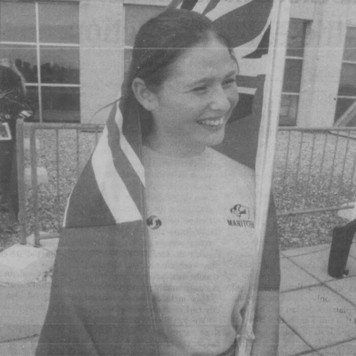 Woman stands holding the Manitoba flag. The flag s draped around her shoulders