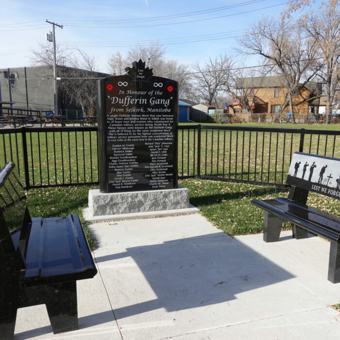 Colour photo of an outdoor space with a black stone monument and two black stone benches
