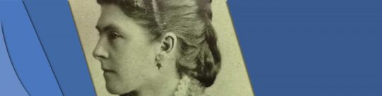 Dufferin Headerbar This is a black and white photo of Lady Dufferin. She has her hair done up and is wearing a fancy button up dress, coat, and bow.