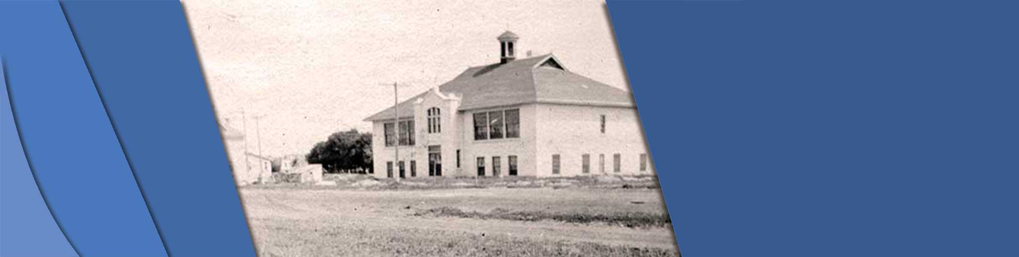 This is a black and white photo of Devonshire School in 1919. it is a tall two story building with windows along each floor. in front of it is an empty field, and there are buildings to its left.