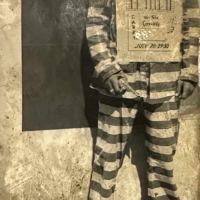 Black and white photo of an employee wearing a jailhouse costume holding a sign