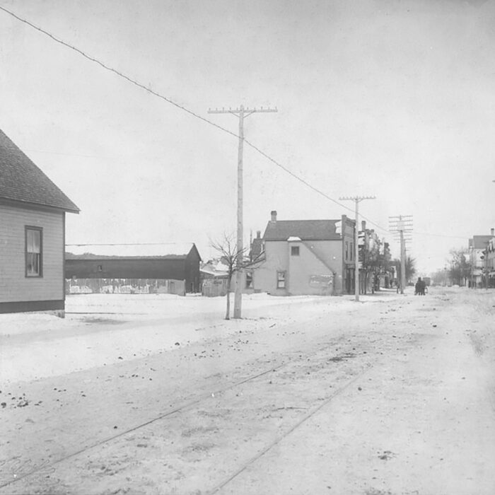 Black and white photo of a street view. There are some small buildings on the left side of the photo