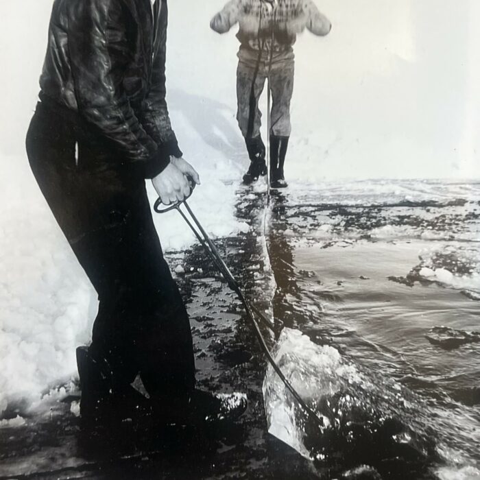 Black and white photo of two men cutting and hauling ice out of the river
