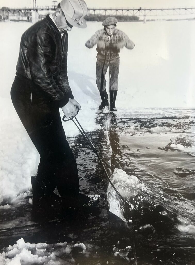 Black and white photo of two men cutting and hauling ice out of the river