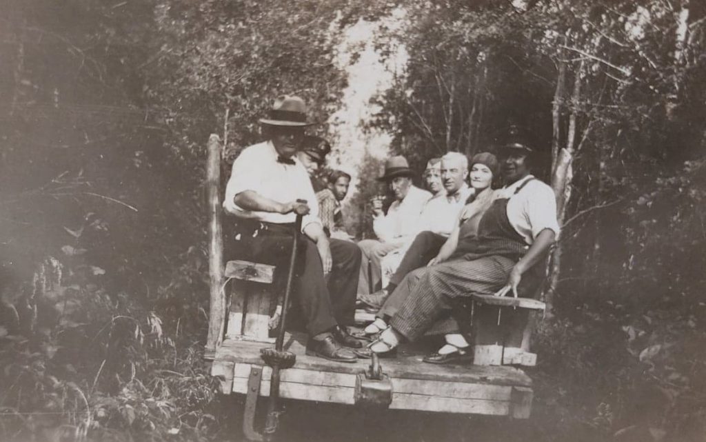 A black and white image of a ferry filled with people. There are trees in the background