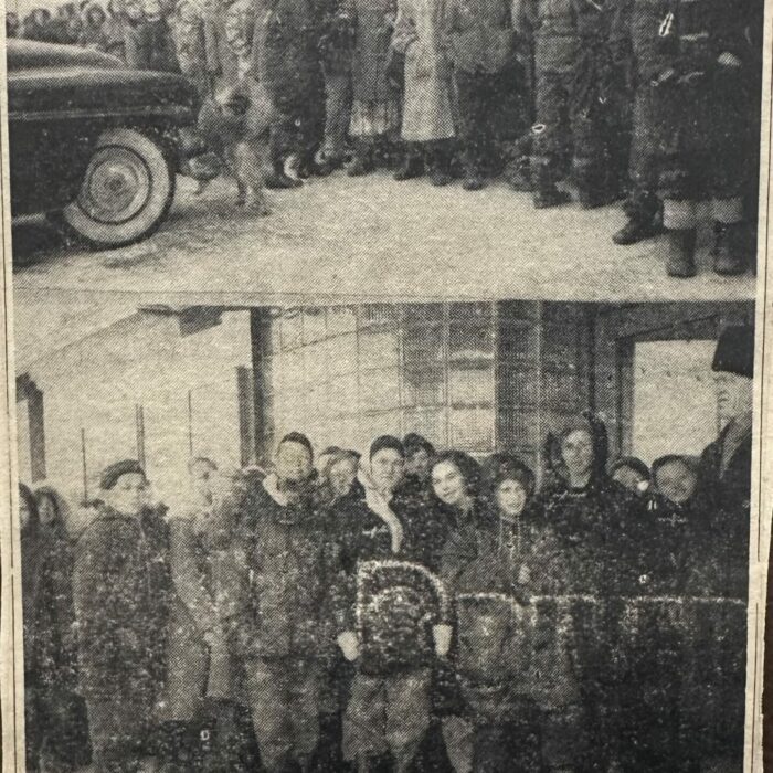 A black and white photo of a group of people standing around a car