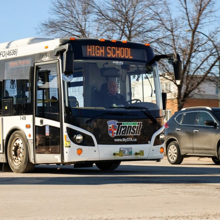 Photo of a bus driving on the road from a three quarter view. A black car is in the lane next to the bus