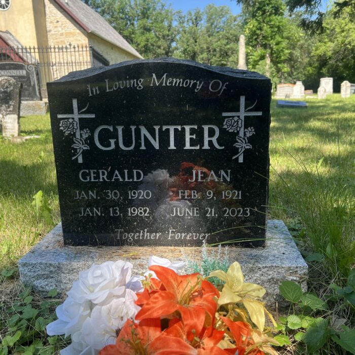 Colour photo of a black headstone which reads ' Gunter'. There is a small church in the background