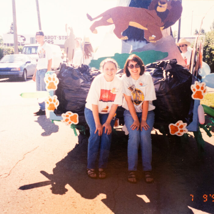 Colour photo of a parade float. Two women sit at the back of the float. The float is decorated to advertise the Lion King
