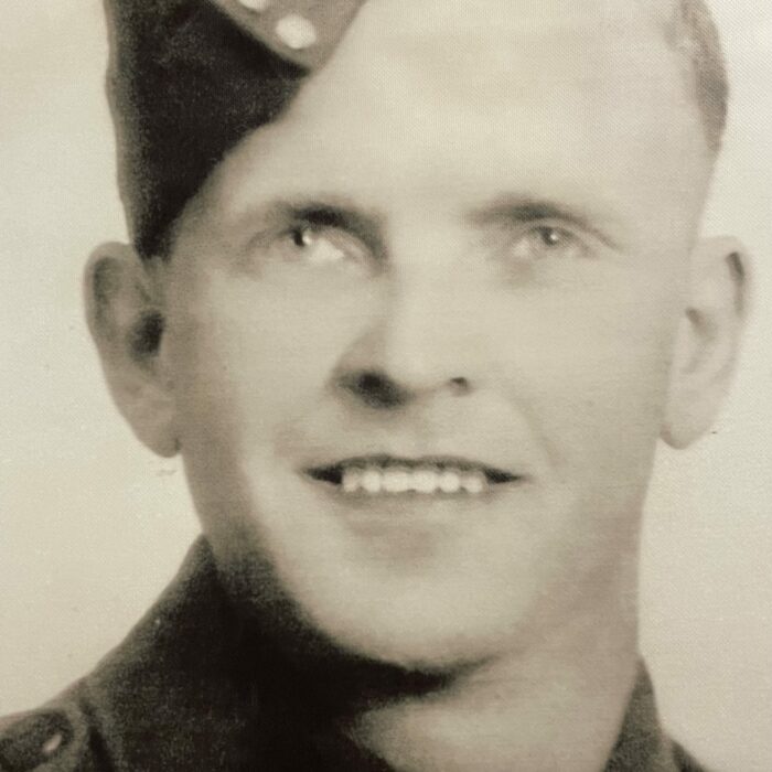 A sepia-coloured image of a soldier. He smiles at the camera and wears a cap and a jacket