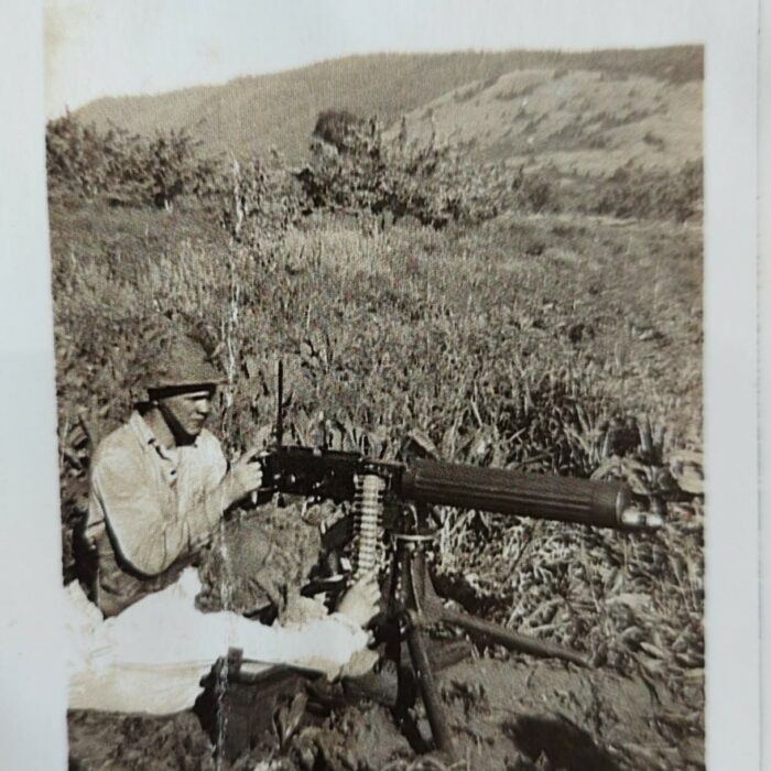 John V. Sinclair and Gun, c1942-1945, Mae Gulewich A black and white photo of a man sitting on the ground holding a rifle