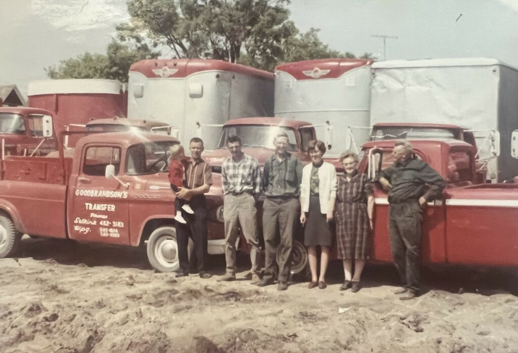 Colour photo of a group of people standing in front of two red trucks