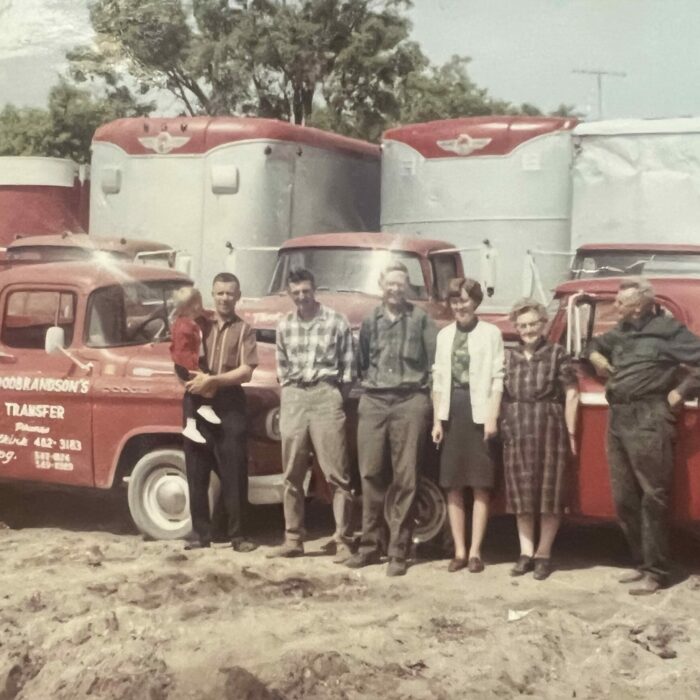 Colour photo of a group of people standing in front of two red trucks