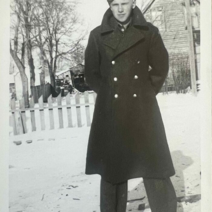 Black and white photo of Lefty standing in the snow. He is wearing a peacoat with double buttons down the front. He is also wearing a hat