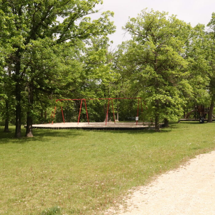 Colour image of a grassy space with trees and a red playground in the distance. In the foreground is a limestone gravel path