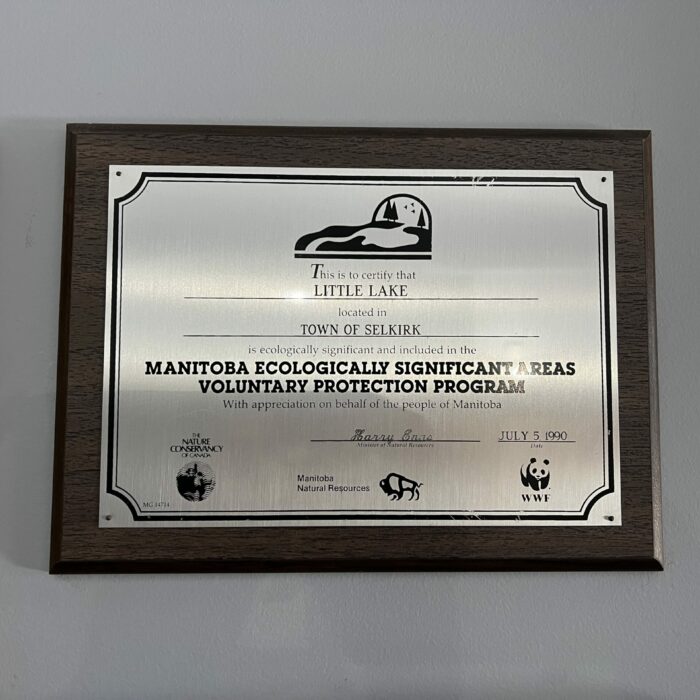 Colour photo of a silver plaque with a wooden frame. The plaque is for Little Lake Park