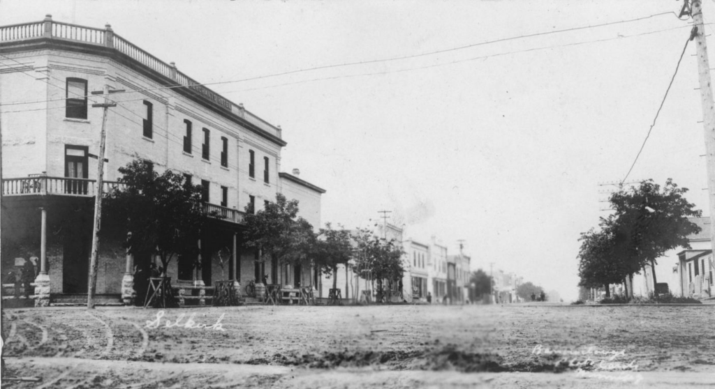 A black and white photo of Manitoba Avenue. The Merchant's Hotel is on the left side of the image