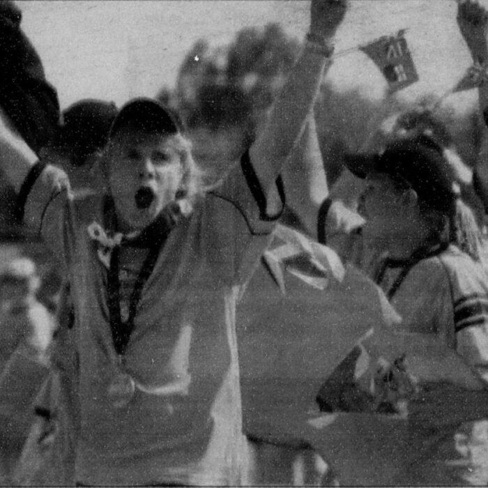 Athlete cheers in victory. They are wearing a ball cap and a medal around their neck