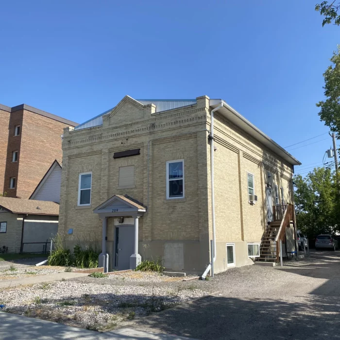 Brick building with archway over door. Side of a building is seen in the background as well as some trees