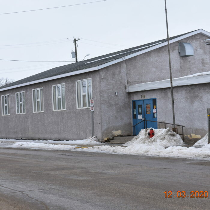 Colour photo of the exterior of memorial hall. The building is grey stucco with white trimmed windows and blue doors