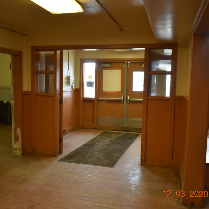 Colour photo of the entryway of a building. there are two sets of double doors leading outside. The doors and trim are painted an orange-brown colour and the walls are yellow.