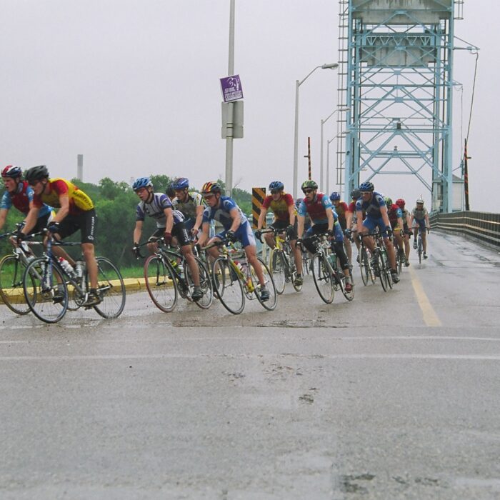 Group of cyclists ride down the road on Eveline Street. The Selkirk Bridge is in the background