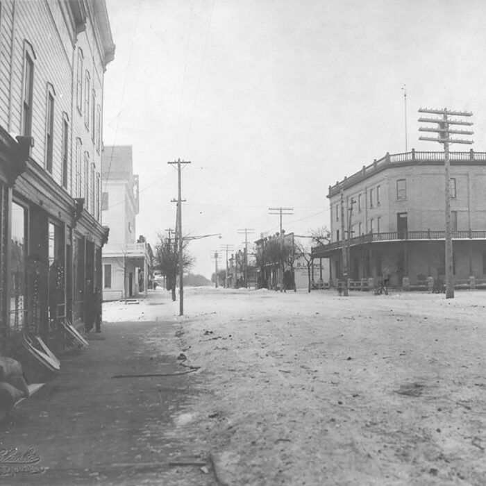 Merchant's Hotel, c1905, JFC Charles, Library and National Archives of Canada Black and white photo of the merchant's hotel from down the street. The street is unpaved and there are telephone poles along the sides of the road. On the left side of the street is a large multi-story building with big windows.