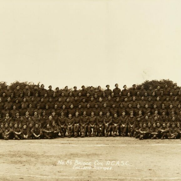 No. 86 Bridge Coy. R.C.A.S.C , England, 1944, Canadian War Museum A long horizontal sepia-coloured image of a group of soldiers. There is a large tree on the right side of the photo. The men in the photo are so small and so many that its hard to see their faces