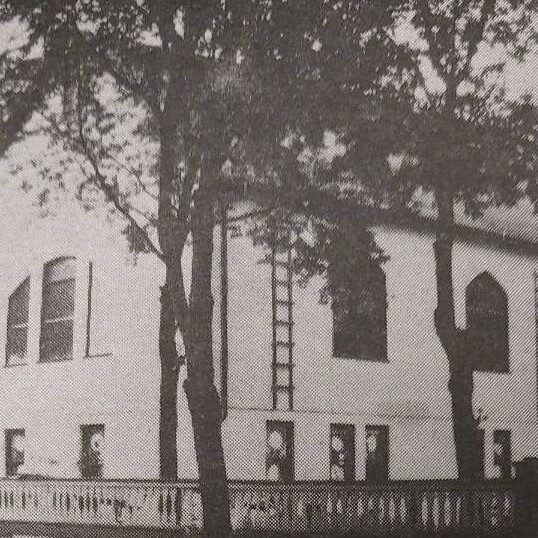 Original Building of the Selkirk United Church, Date Unknown, Selkirk Enterprise Centennial A black and white photo of a church from behind a few trees