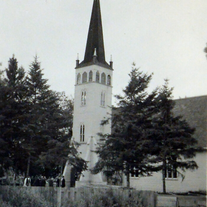 Original Christ Church on McLean Ave, 1950, Archives of Manitoba George Harris Fonds Black and white image of a white church with a tall steeple. There are trees on either side of the church