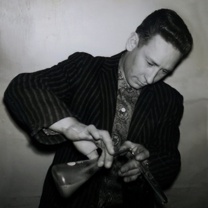 Podruchny Chemistry Instructor, 1970, Thomas Podruchny Black and white image of a Tom pouring from a beaker. He is wearing a black jacket and looks down intently at the beaker