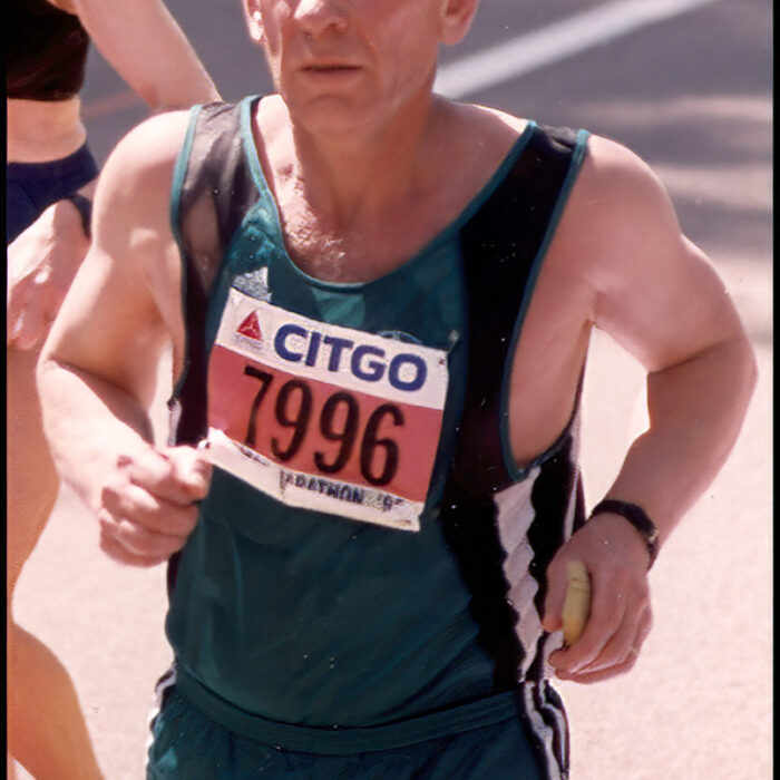 Podruchny at Boston, 1993, Thomas Podruchny Three quarter angle photograph of a man running. He is wearing a green and black shirt with green shorts. The number 7996 is pinned to his shirt. The letters 'Boston MA' is printed in the bottom right corner