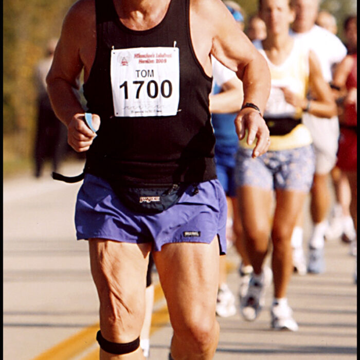 Podruchny at Milwaukee, 2000, Thomas Podruchny Tom running with others in the background. He is wearing a black shirt and purple shorts. The number 1700 is pinned to his shirt. The letters 'Milwaukee, WI' are printed in the bottom right corner