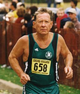 Image of Tom running towards the camera he is wearing a green shirt and green shorts. The number 658 is pinned to his shirt