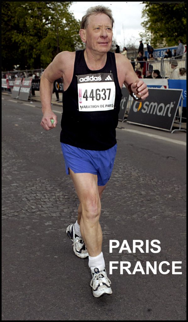Man running towards camera wearing a balck shirt and blue shorts, number 44637 is pinned to his shirt. 'Paris' is printed across the bottom of the image