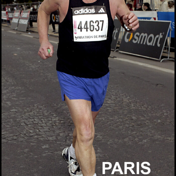 Podruchny at Paris France, 1992, Thomas Podruchny Man running towards camera wearing a balck shirt and blue shorts, number 44637 is pinned to his shirt. 'Paris' is printed across the bottom of the image